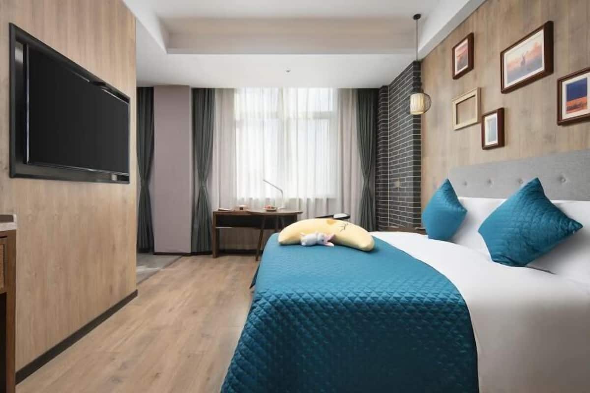 A hotel room with a bed, a desk, a TV, and a window with curtains.