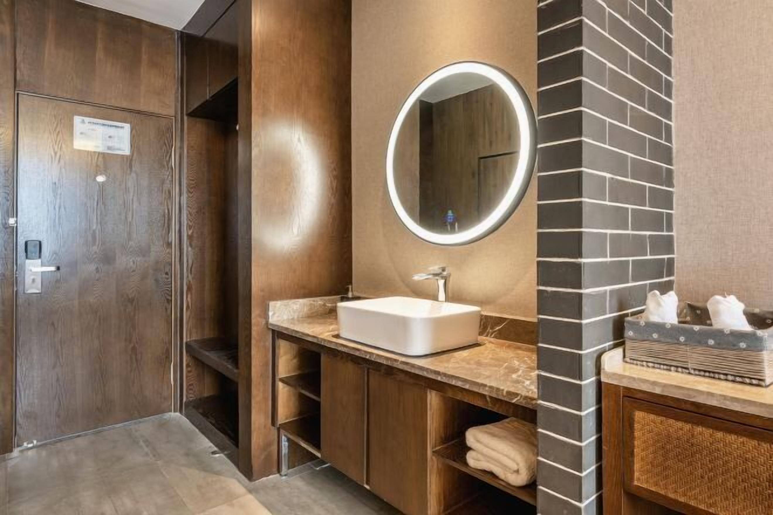 A modern bathroom with a wooden vanity, a white sink, a mirror with a light, and a towel rack.