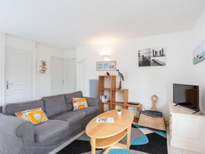 A modern living room with a grey sofa, a wooden coffee table, and a TV on a white cabinet.