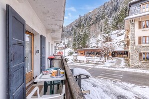 Un balcón con una mesa dispuesta para el desayuno, con vista a una montaña nevada y un pequeño pueblo.