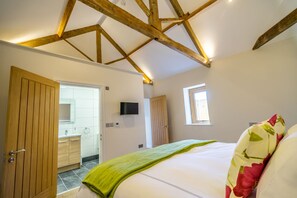 A bedroom with a wooden ceiling, a bed with a green blanket, a TV on the wall, and a window.