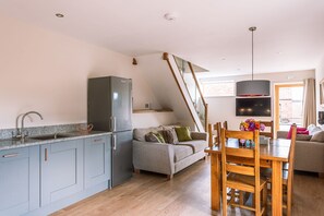 A modern kitchen with a built-in fridge, grey cabinets, and a wooden dining table with chairs.