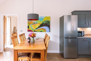 A dining area with a wooden table, chairs, a vase of flowers, and a colorful painting on the wall.