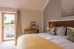 A hotel room with a large bed, a wooden headboard, a dresser, a mirror, and a view of a garden through an open door.