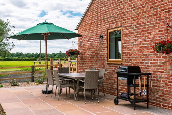 A patio with a table and chairs, a grill, and hanging flower baskets.
