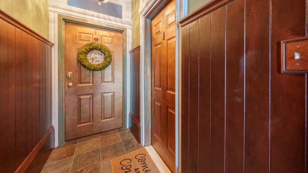 Une porte en bois, ornée d’une guirlande et surmontée d’un paillasson.