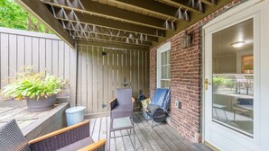 Une terrasse couverte, aménagée avec des meubles en osier, une plante en pot et un barbecue.