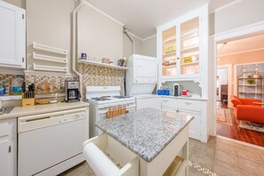 Eine moderne Küche mit weißen Schränken, einer Granit Arbeitsplatte und einem eingebauten Ofen. Es gibt einen Essbereich mit einem weißen Tisch und Stühlen.