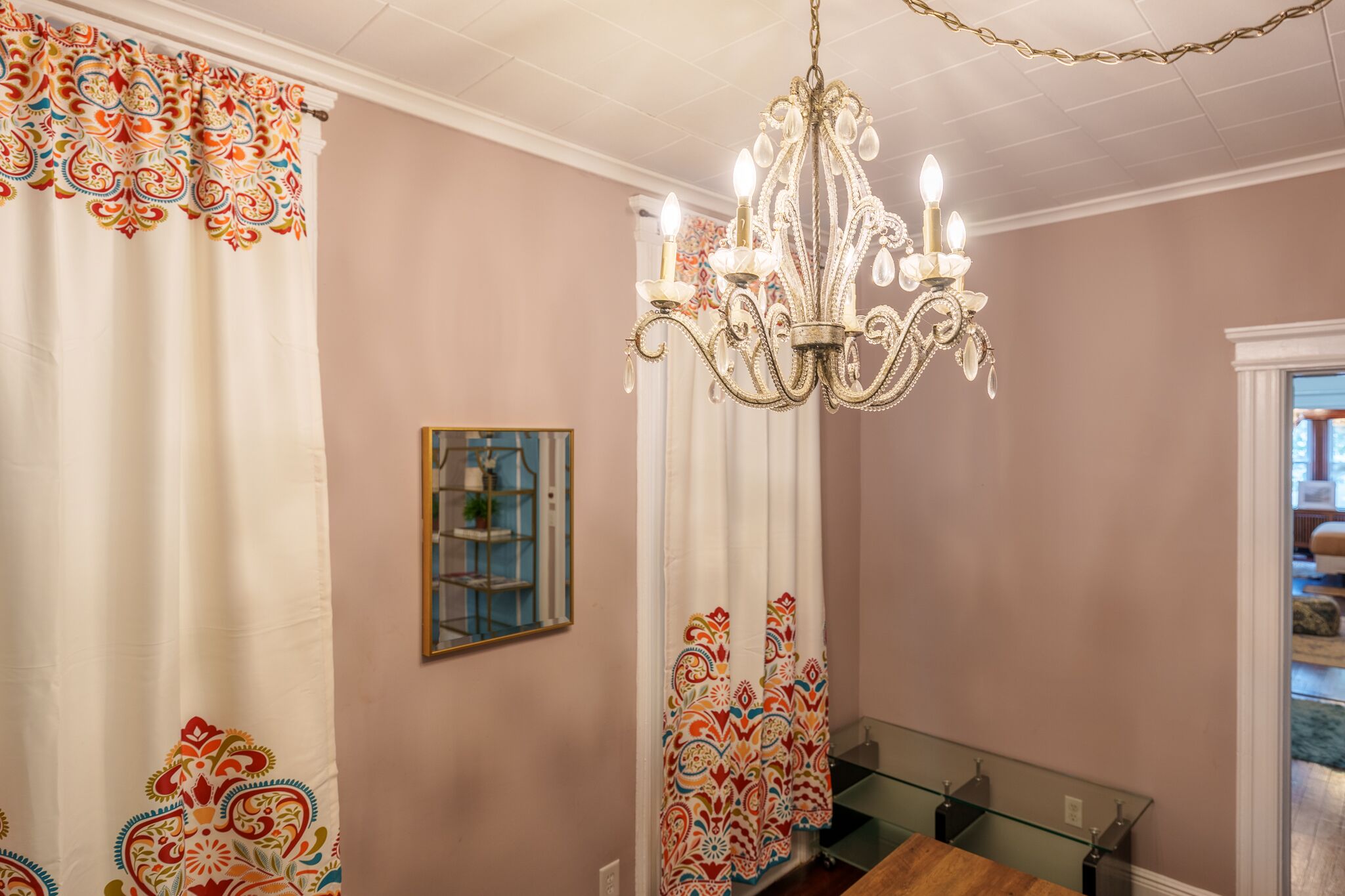 A dining area with a chandelier, patterned curtains, and a glass-top table.