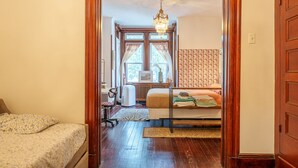 Une chambre à coucher avec un lit en bois, un bureau et une chaise. Il y a une fenêtre avec des rideaux et un radiateur.