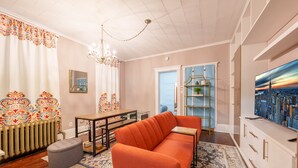 Un salon comprenant un canapé, une table, un lustre, un radiateur, un téléviseur et une bibliothèque.