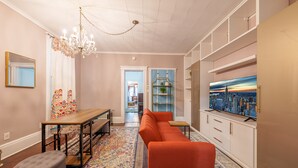 Un salon moderne avec un canapé, une table basse, un lustre et un téléviseur diffusant une vue sur la ville.