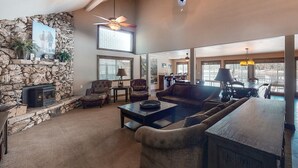 Un salon spacieux avec une cheminée en pierre, des sièges confortables, une grande fenêtre et un ventilateur de plafond.