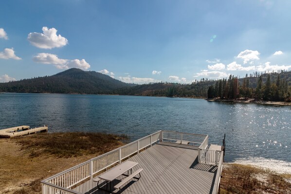 A wooden deck with picnic tables overlooking a calm lake, surrounded by forested hills.