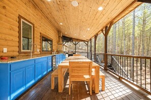 Eine Holzhütte mit einer Veranda, einem Esstisch und blauen Schränken.