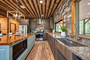 Una cocina moderna con vigas de madera, encimeras de granito, electrodomésticos de acero inoxidable y un ventanal grande.