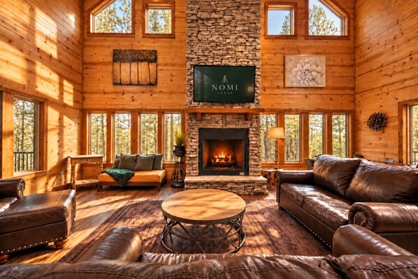 A lodge interior with a stone fireplace, leather furniture, and large windows.