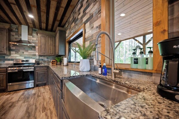 A modern kitchen with granite countertops, stainless steel appliances, and a large window. - Sleeps 28! • Loaded w/ Amenities • Mins from Lake! (Broken Bow)