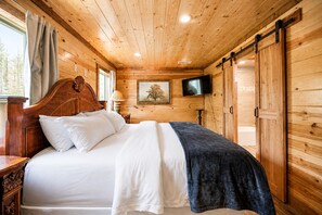 Een slaapkamer met houten lambrisering, een bed, een televisie en een schuifdeur.