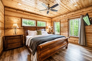 A wooden cabin bedroom with a bed, nightstands, a ceiling fan, and large windows.