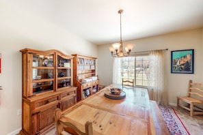 A dining area with a wooden table, chairs, a chandelier, and a bookshelf.