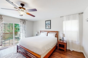 A bedroom with a wooden bed, a ceiling fan, a nightstand, and a window with curtains.
