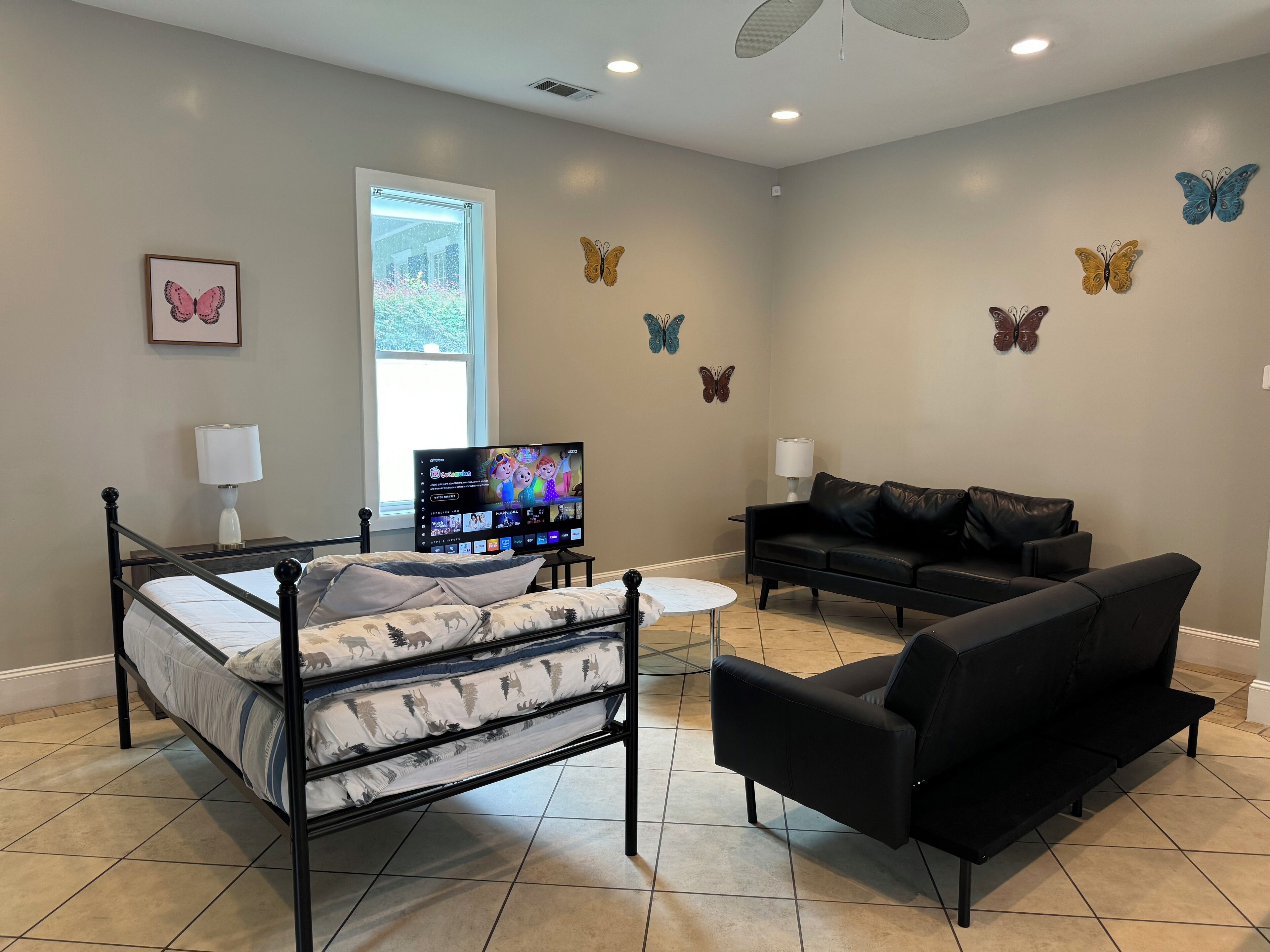 Un dormitorio con una cama, un sofá negro, un televisor y adhesivos de mariposas en la pared.