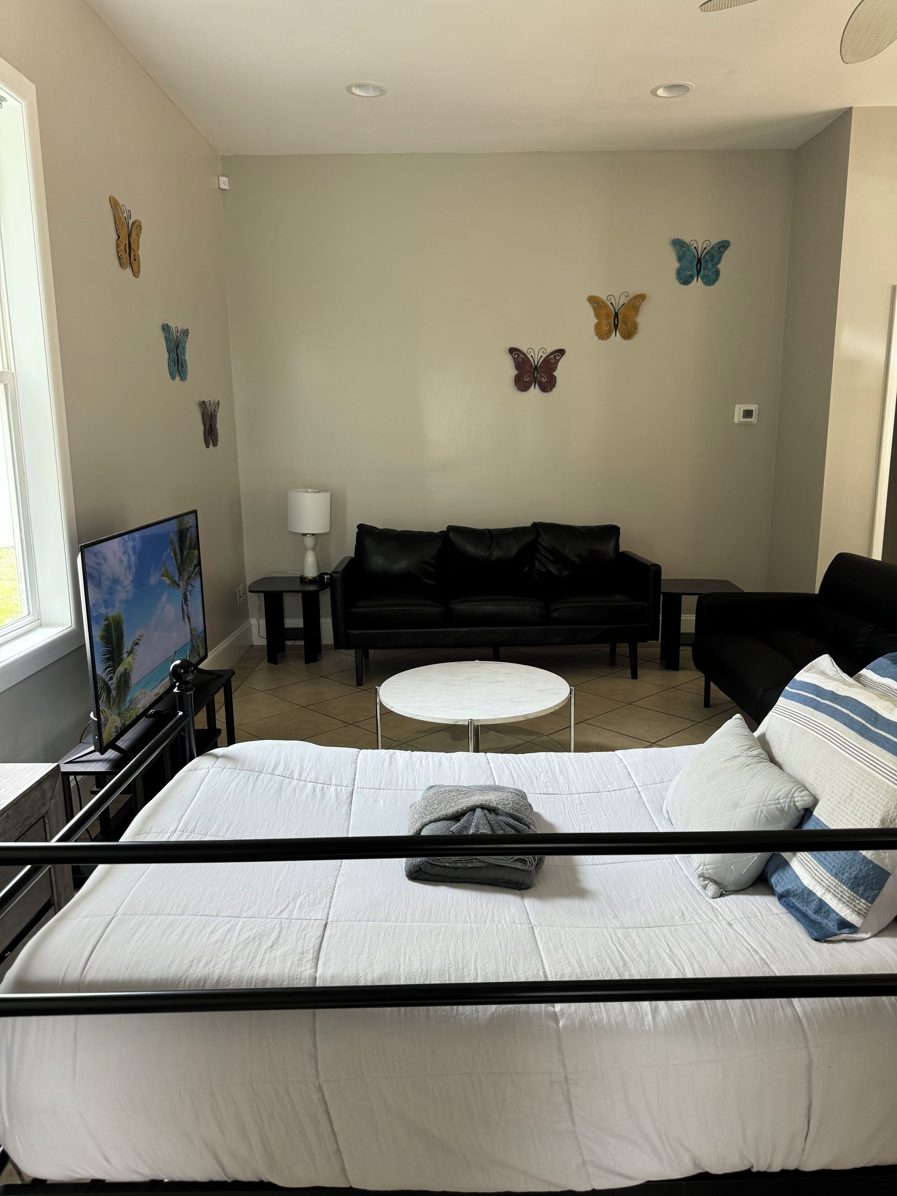 Un dormitorio con cama, sofá negro, una pequeña mesa redonda y decoración de mariposas en la pared.