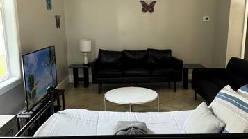 Un dormitorio con cama, sofá negro, una pequeña mesa redonda y decoración de mariposas en la pared.