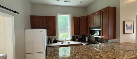 A modern kitchen with granite countertops, wooden cabinets, a built-in microwave, and a large window.