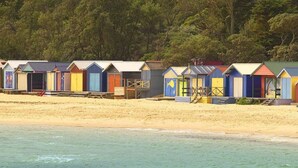 Une rangée de cabanes de plage, avec une plage de sable et l’eau au premier plan.