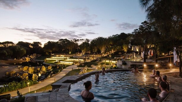 Un espace piscine où des personnes se détendent, entouré de jardins aménagés et de sentiers.