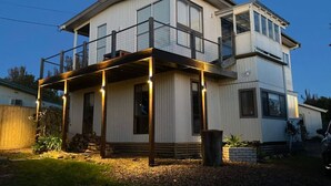 A two-story house with a balcony, a visible chimney, and a stack of firewood outside.