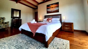 A bedroom with a large bed, wooden headboard, a painting on the wall, a nightstand, and a chair.
