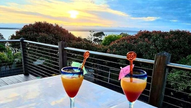 Two cocktails on a table with a view of the ocean and sunset.