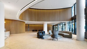 A spacious lobby with a curved ceiling, a central seating area with sofas and chairs, and large windows providing natural light. - Riverside Views Melbourne - WiFi-Netflix (Docklands)