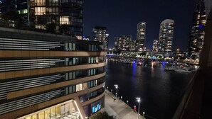 A modern building with a curved facade and large windows, overlooking a river with boats and city lights in the background. - Riverside Views Melbourne - WiFi-Netflix (Docklands)