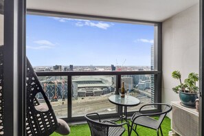 A balcony with a view of a stadium, a table with chairs, and a potted plant.