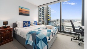 A bedroom with a large bed, a nightstand, a desk, and a chair. There is a large window with a view of buildings and a bridge. - Water Views Melbourne CBD - WiFi - Netflix (Melbourne)