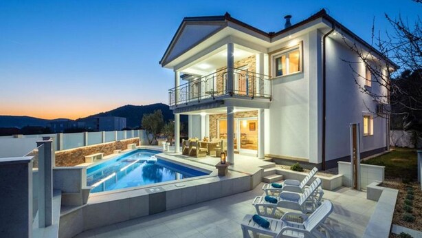 A modern two-story house with a swimming pool, outdoor seating, and a balcony.