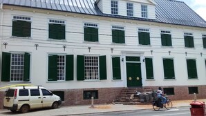 Valkoinen rakennus, jossa on vihreät ikkunaluukut ja tiilestä tehty sokkeli.
