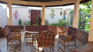 A covered outdoor seating area with wicker furniture and patterned cushions, surrounded by a tiled floor and decorative wall art. - Full AirCon- 3Bed Villa- A/c- WiFi- HotWater (Freetown)