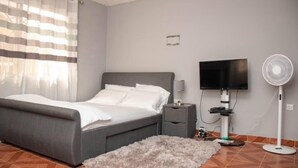 A bedroom with a bed, bedside table, TV, and a standing fan. - Full AirCon- 3Bed Villa- A/c- WiFi- HotWater (Freetown)