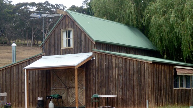 A rustic barn with a green roof, a covered porch, and a table and chair set outside.