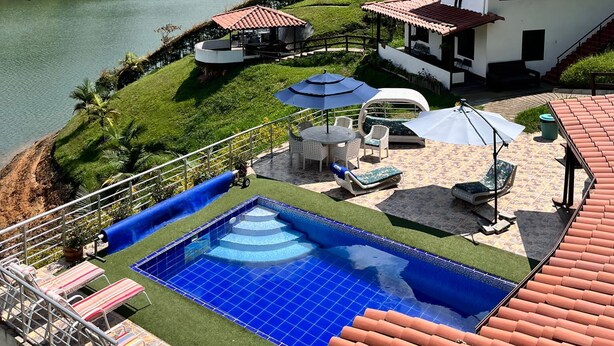 Zona de piscina con vistas a un lago, rodeada de viñedos en terrazas y una colina.