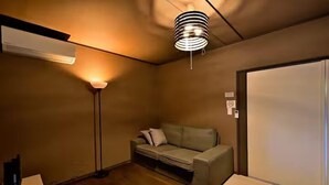 Una habitación pequeña, con poca luz, que tiene un sofá, una lámpara de pie y un accesorio de iluminación en el techo.