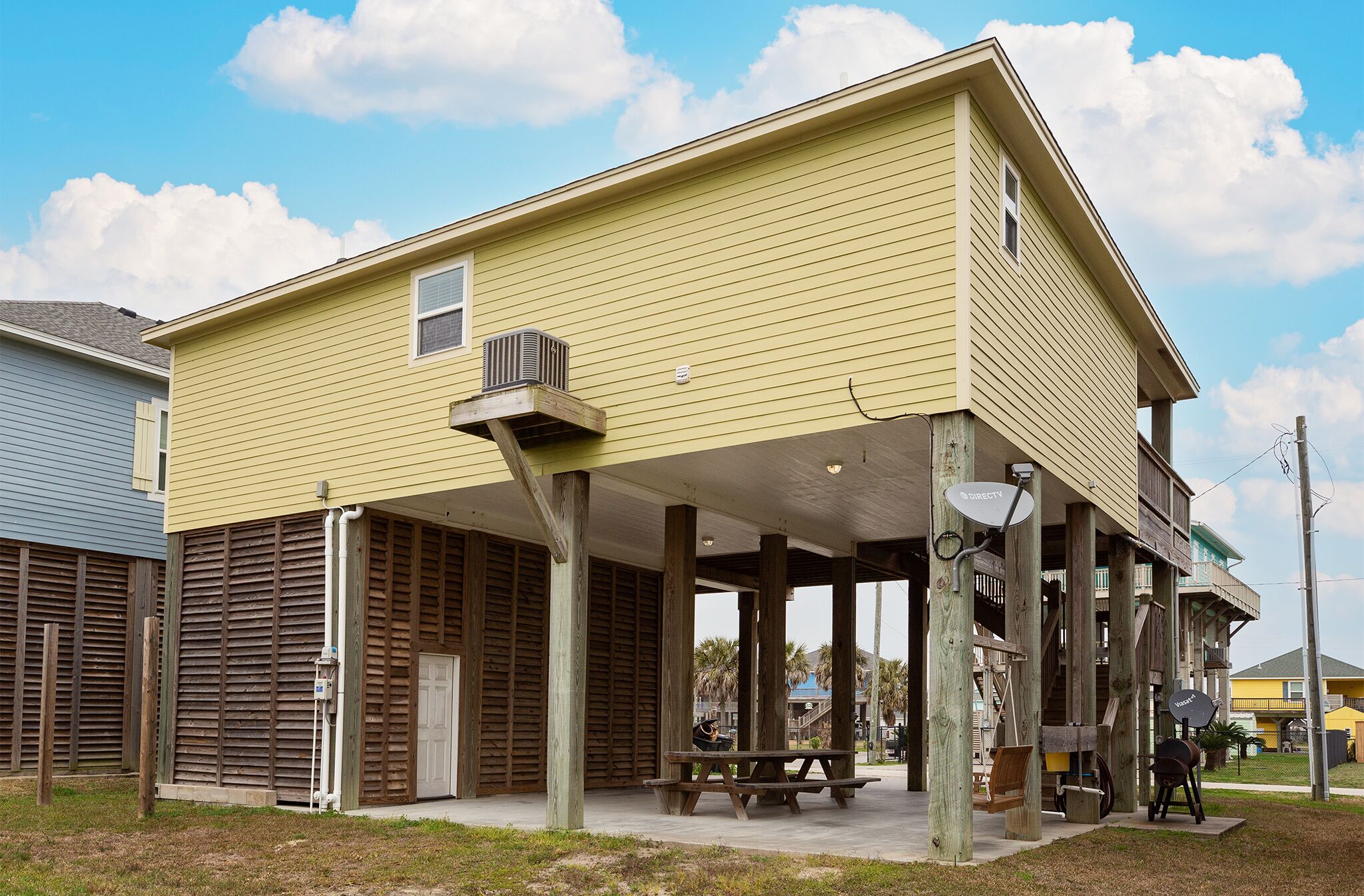 A yellow building with a covered porch, wooden shutters, and a satellite dish.