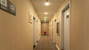 A hotel hallway with doors on both sides, a fire extinguisher, and a sign indicating the direction to the elevator. - 7Days Inn Shenzhen Shajing Metro Station public square (Shenzhen)