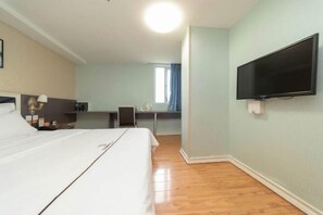 Ett hotellrum med en säng, ett skrivbord, en stol, en tv och ett fönster med gardiner.