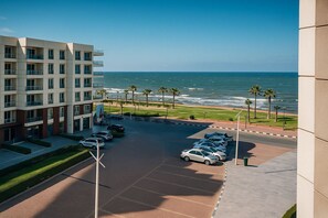 A modern hotel with a parking lot, a view of the ocean, and a landscaped area with palm trees.